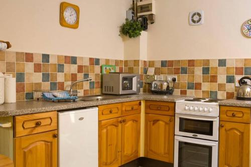 a kitchen with wooden cabinets and a white stove top oven at Sherbourne Cottage, Seven Springs Cottages in Cheltenham