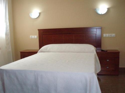 1 dormitorio con cama blanca y cabecero de madera en Hostal el Altozano, en Montánchez