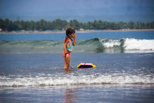a little girl standing in the ocean with a surfboard at Jelajah Batukaras in Batukaras