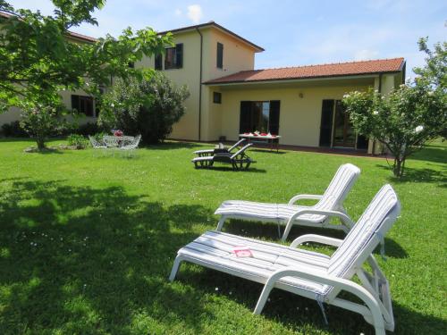 three white chairs sitting in the grass in front of a house at Casa con piscina campo da tennis vicino al mare e alle Cinque Terre in Ameglia