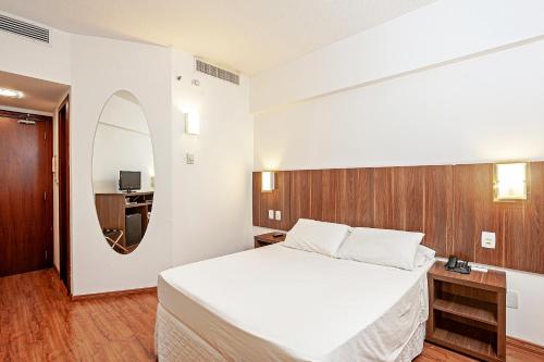 a bedroom with a large white bed and a mirror at Firenze Business Hotel in Palhoça