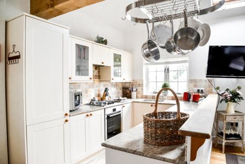 uma cozinha com armários brancos e um cesto no balcão em Chichester Cottage em Funtington