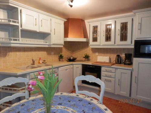 uma cozinha com armários brancos e uma mesa com flores em Maison Studios & Appartements Les 4 Vents em Luc-sur-Mer