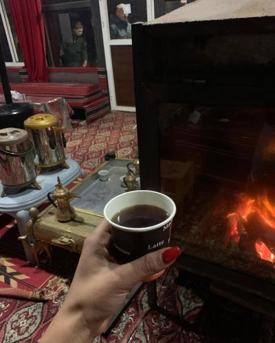 a person holding a cup of coffee in front of a fireplace at golden day in Wadi Rum