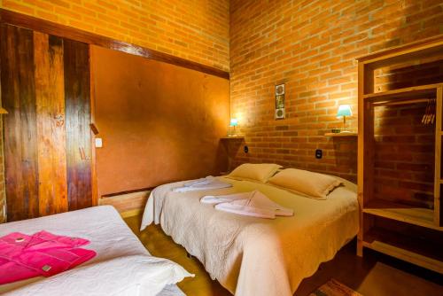 a bedroom with two beds and a brick wall at Hospedaria Estação Píccola No quintal da Pedra do Baú in São Bento do Sapucaí