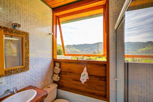a bathroom with a window and a toilet and a sink at Hospedaria Estação Píccola No quintal da Pedra do Baú in São Bento do Sapucaí