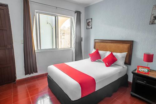 a bedroom with a bed with red pillows and a window at Hotel Dpas 52 in Mérida