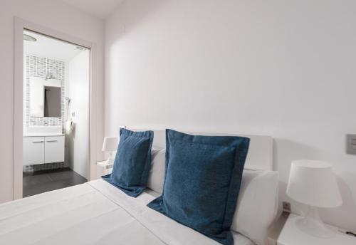 a white bedroom with blue pillows on a bed at Apartamentos Globus by Be Alicante in Alicante