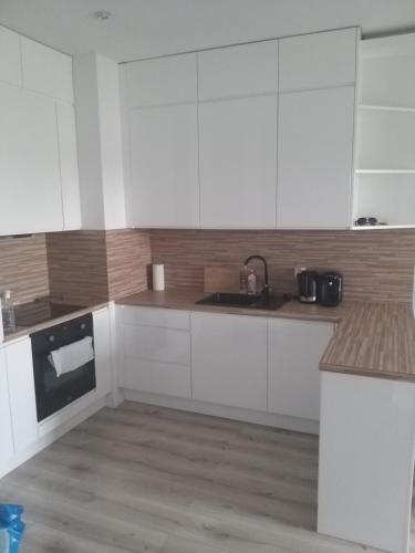 uma cozinha com armários brancos e um lavatório em Apartament Nowa Letnica em Gdansk