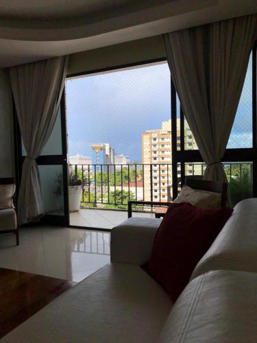 a living room with a couch and a large window at Apartamento amplo, arejado e confortável - Mínimo 3 noites in Ilhéus