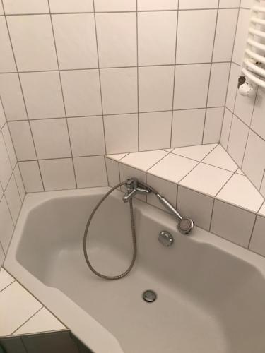 y baño de azulejos blancos con bañera y manguera. en Sanierte möblierte Altbauwohnung am Waldrand für bis zu 6 Personen en Borkheide