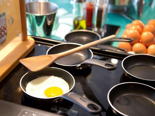 a stove top with pans with an egg in them at Novotel Senart Golf De Greenparc in Saint-Pierre-du-Perray