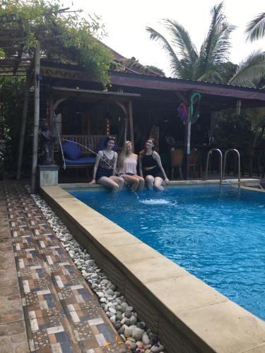 three women sitting on the edge of a swimming pool at Breeze Villa in Nusa Lembongan