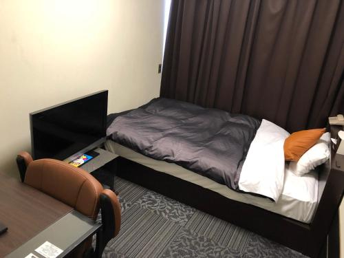 a small bedroom with a bed and a desk with a computer at Business Stay in Satsumasendai