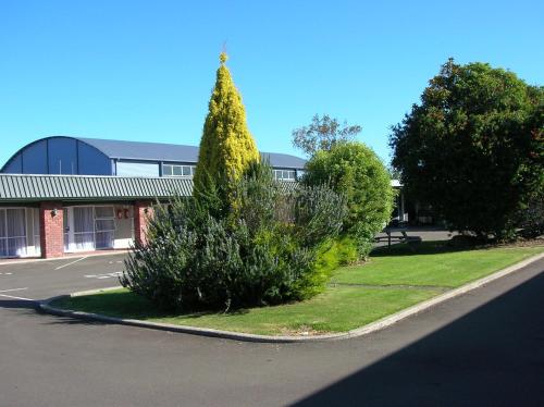 a bush in front of a building with a tree at Palmerston North Motel in Palmerston North
