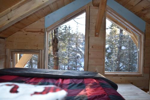 uma cama num quarto com duas janelas grandes em Bois Rond Expérience em Saguenay