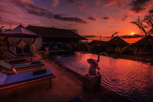 a pool with a statue in front of a sunset at D'Coin Lembongan in Nusa Lembongan