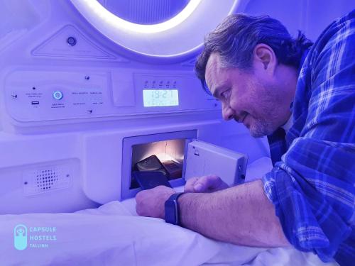 a man laying in a hospital bed with a phone at Capsule Hostels Tallinn in Tallinn