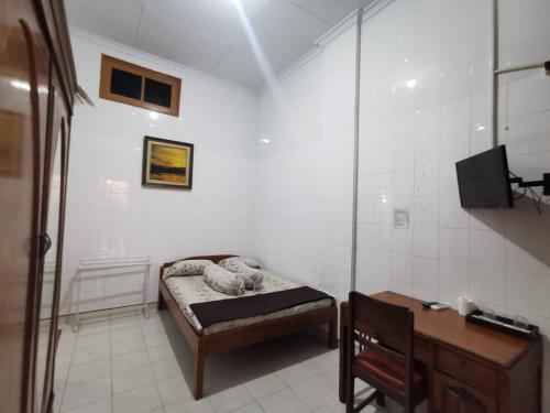 Habitación pequeña con cama, escritorio y TV. en Hotel Paviljoen, en Surabaya