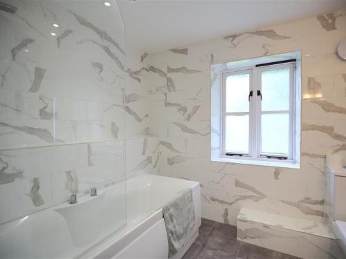 a white bathroom with a tub and a window at The Cottage in Saint Briavels