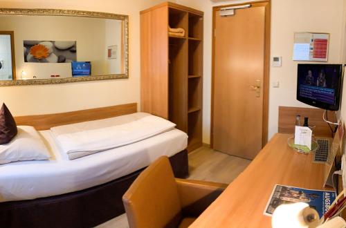 a room with a bed and a desk and a television at City Hotel Ost am Kö in Augsburg