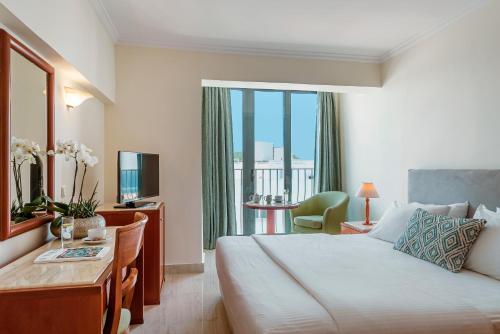 a hotel room with a bed and a desk and a window at Mitsis La Vita in Rhodes Town