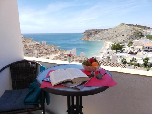 a table with a book and a bowl of fruit on a balcony at Hotel Burgau Turismo de Natureza in Burgau