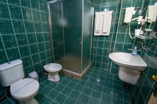 Baño de azulejos verdes con aseo y lavamanos en Hotel Kristal Palas, en Prilep