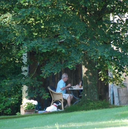 un homme assis à une table sous un arbre avec un chien dans l'établissement Bergerie de la Moutonnière, au Pin