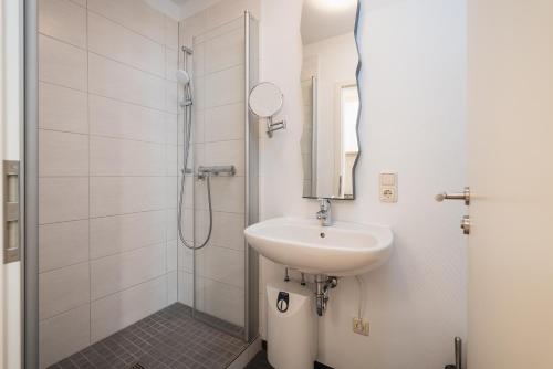 La salle de bains blanche est pourvue d'un lavabo et d'une douche. dans l'établissement Das Handtuchhaus - Wohnen im schmalsten Haus - Mittendrin, à Heringsdorf