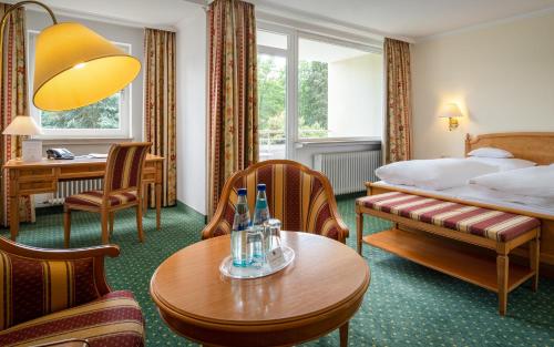 オーバーウルゼルにあるParkhotel am Taunusのベッド、テーブル、椅子が備わるホテルルームです。