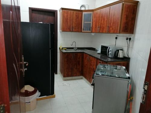 Una cocina con gabinetes de madera y un refrigerador negro. en Discovery Furnished Apartments (Al-Amerat), en Sayḩ adh Dhabi