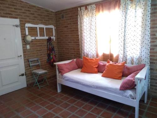 Habitación con cama con almohadas de color naranja y ventana. en Casa Dos, casita de campo en Alta Gracia