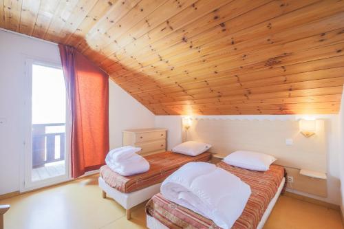 deux lits dans une chambre avec un plafond en bois dans l'établissement Residence Les Chalets de Puy Saint Vincent - maeva Home, à Puy-Saint-Vincent