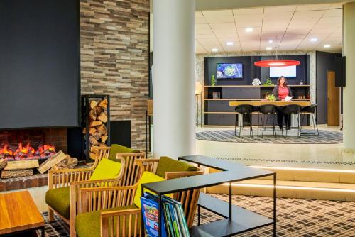 a woman sitting at a table in a lobby with a fireplace at Novotel Senart Golf De Greenparc in Saint-Pierre-du-Perray