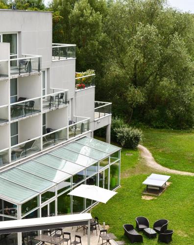 a building with a table and chairs and an umbrella at Novotel Senart Golf De Greenparc in Saint-Pierre-du-Perray