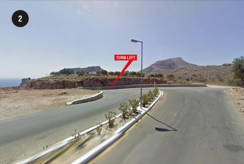 a road with a sign that reads turn left at Villa Stavros in Archangelos