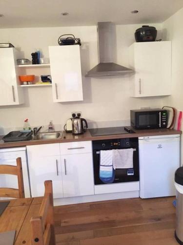 una cucina con armadi bianchi, lavandino e forno a microonde di Orchard Cottage a Canterbury