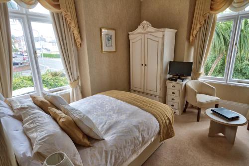 a bedroom with a bed and a dresser and windows at Holcombe House Guest House in Llandudno