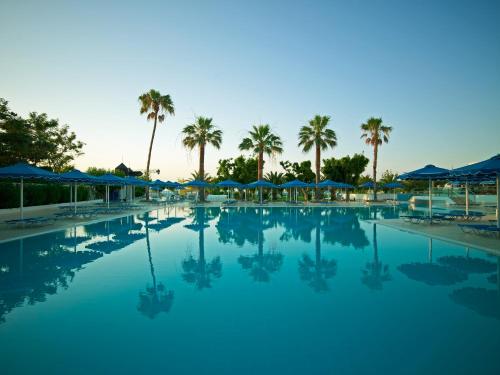 a large swimming pool with palm trees and blue umbrellas at Mitsis Faliraki in Faliraki