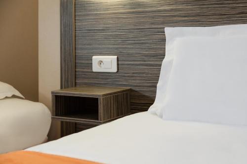 a bedroom with a bed and a nightstand next to a bed sidx sidx sidx at The Originals City, Hôtel L'Acropole, Saint-Etienne Sud in La Ricamarie