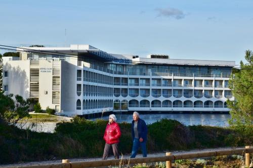 an older couple walking in front of a building at Hotel Club Le Plein Sud Vacances Bleues in Hyères