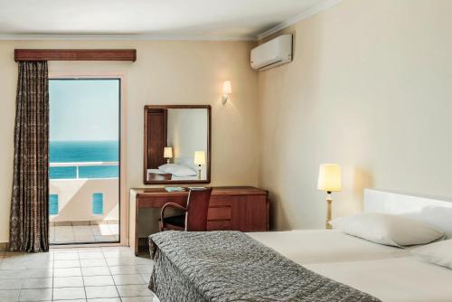 a hotel room with a bed, chair and a window at Mitsis Family Village Beach Hotel in Kardamaina