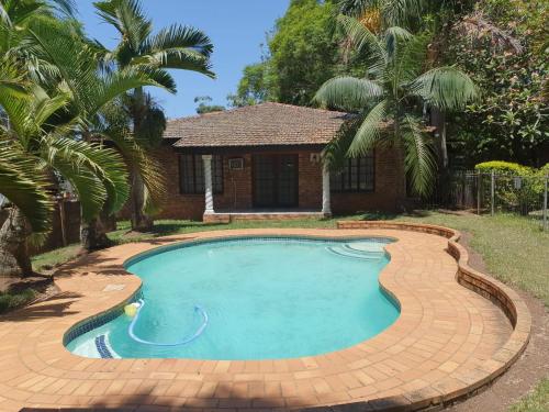 a swimming pool in front of a house with palm trees at Carsdale country lodge in Empangeni