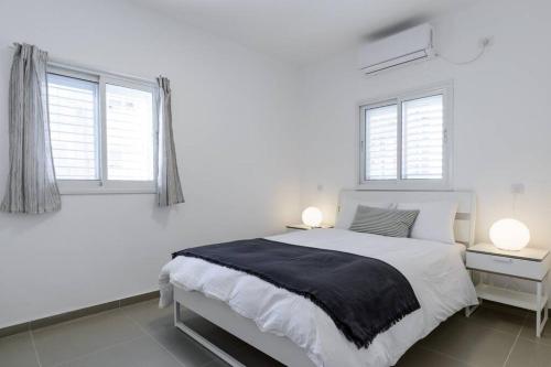 - une chambre blanche avec un lit et 2 fenêtres dans l'établissement Botiuqe apartment . 100 meters from the beach, à Tel Aviv