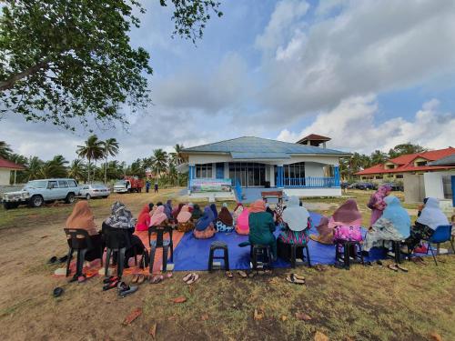 a group of people sitting around a table in front of a house at ALA Beach Lodge - Ketapang Homestay in Kota Bharu