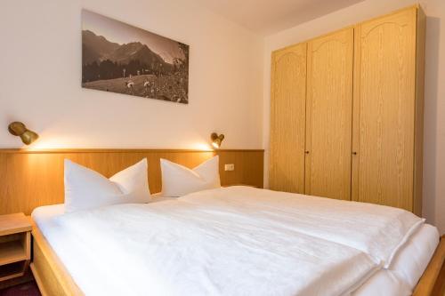 a bedroom with a white bed with a wooden cabinet at Landhaus Almrausch in Mittelberg