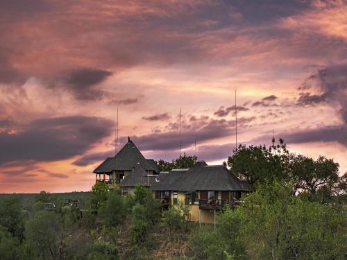 Makumu Private Game Lodge في محمية كلاسيري الطبيعية الخاصة: منزل يجلس على قمة تل تحت السماء الغائمة