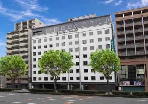 a white building with trees in front of a street at Urban Hotel Kyoto Gojo Premium in Kyoto