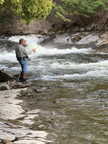 a man standing in a river holding a fishing rod at Pine Crest Motel & Cabins in Barton